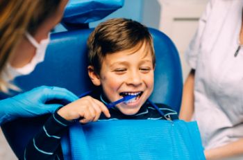 Smiling boy in dental chair brushing his teeth