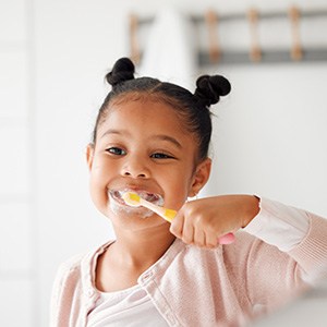 Child smiling while brushing teeth in bathroom