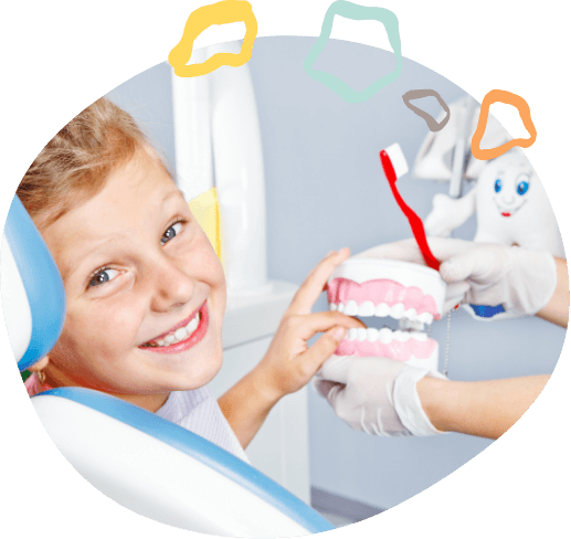 Child smiling in dental chair while dentist shows them a model of the teeth